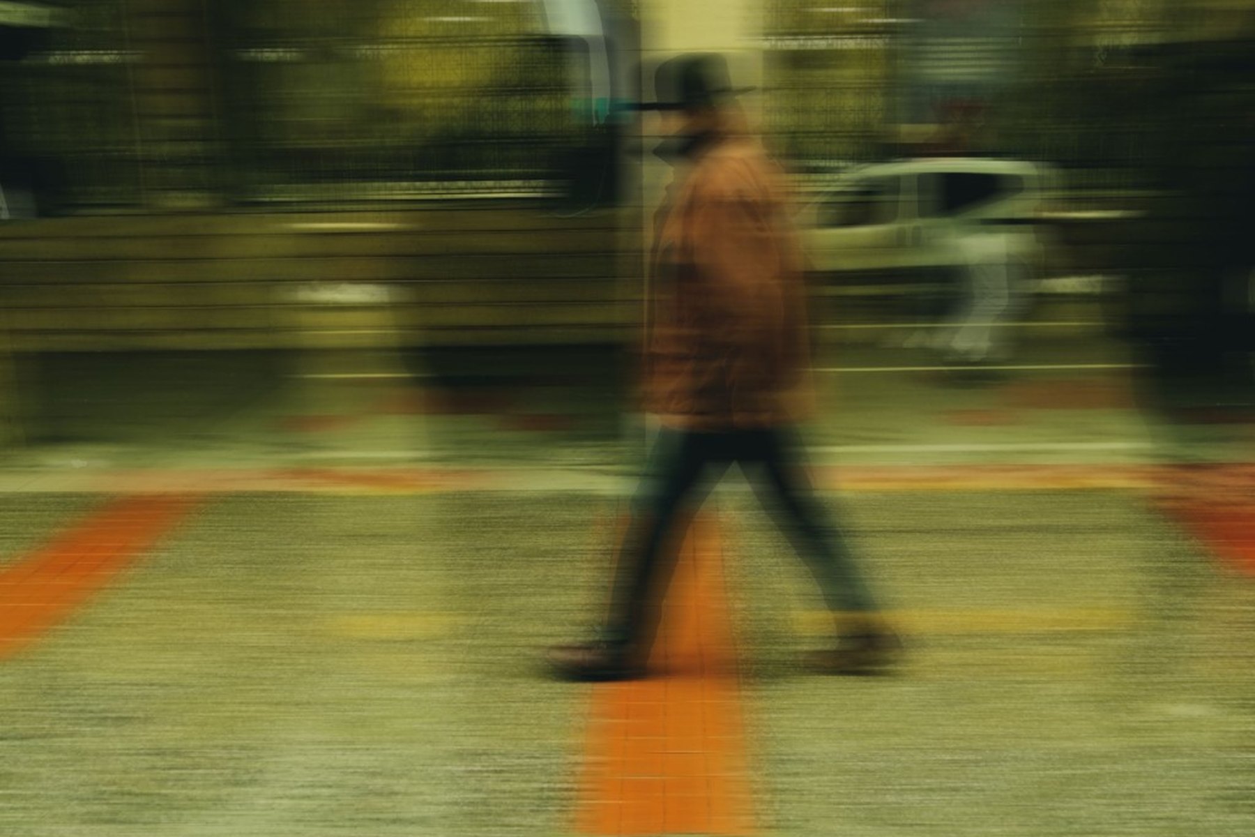 A walker crossing orange pavement stripes, dissolved by a long exposure