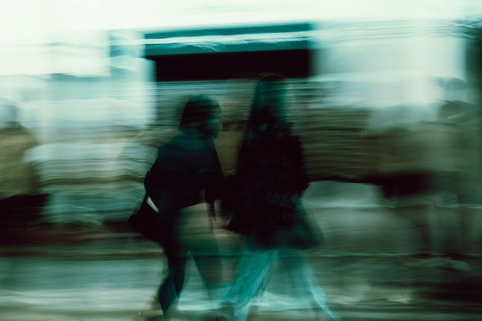 Walking figures streaked into teal light on a night street