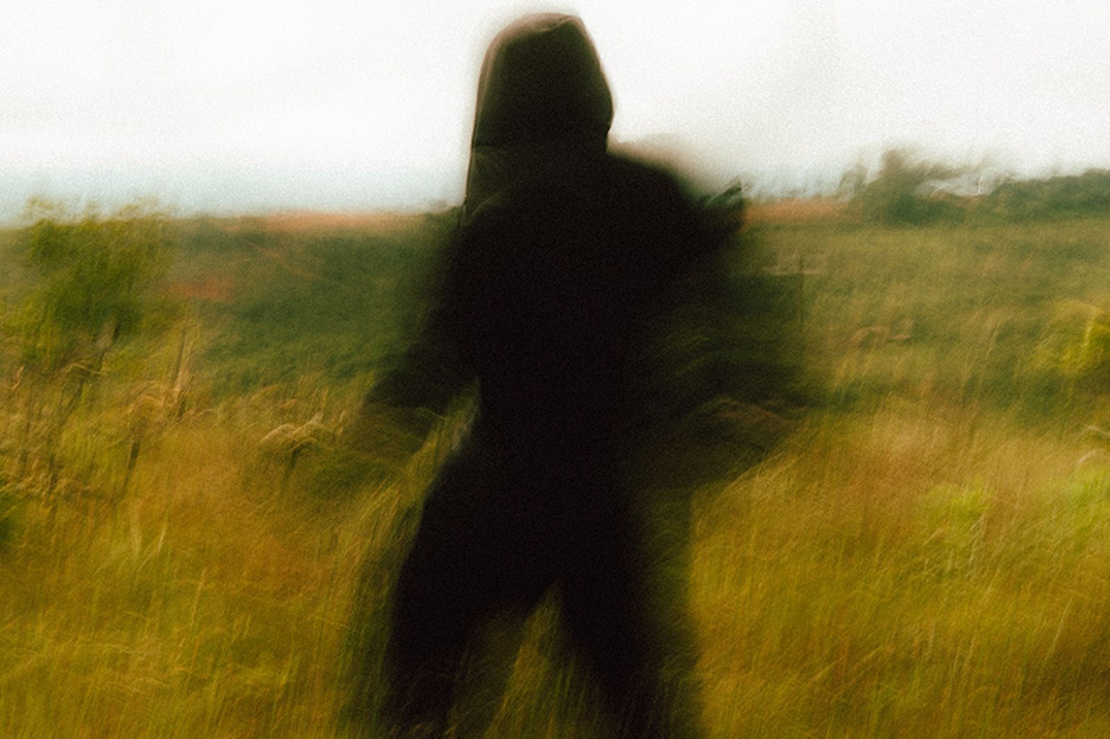 A hooded figure in tall grass, dissolved by a long exposure