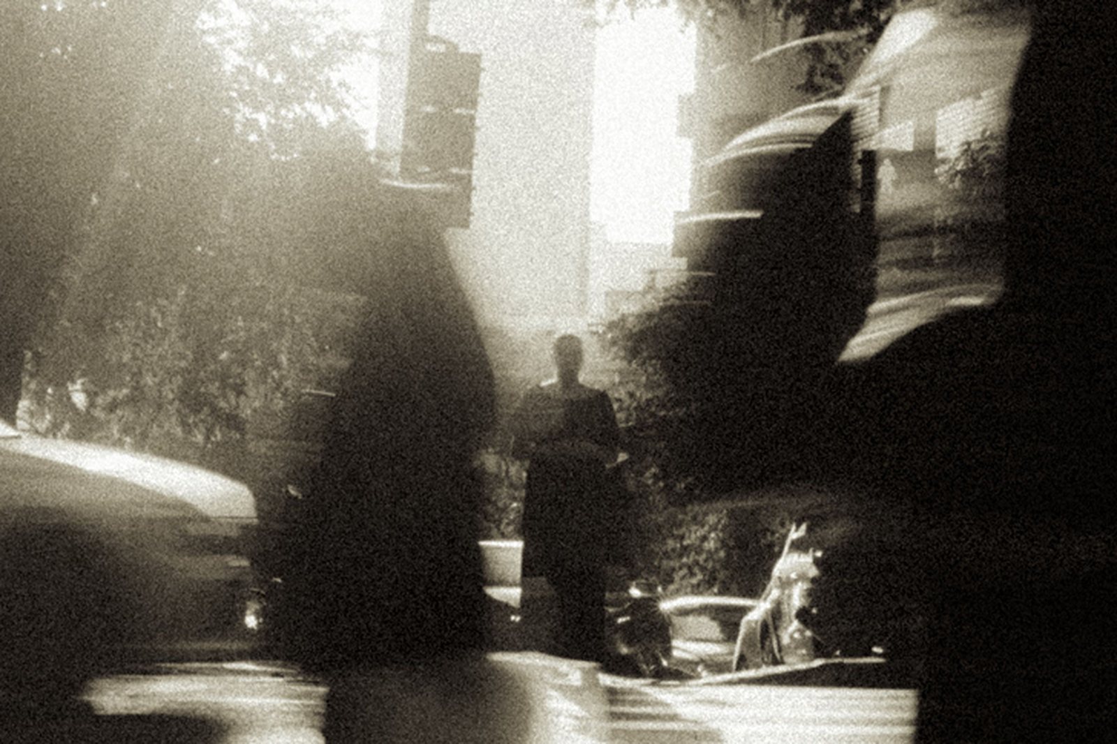 A still figure on a blurred city street, grain and flare washing the frame