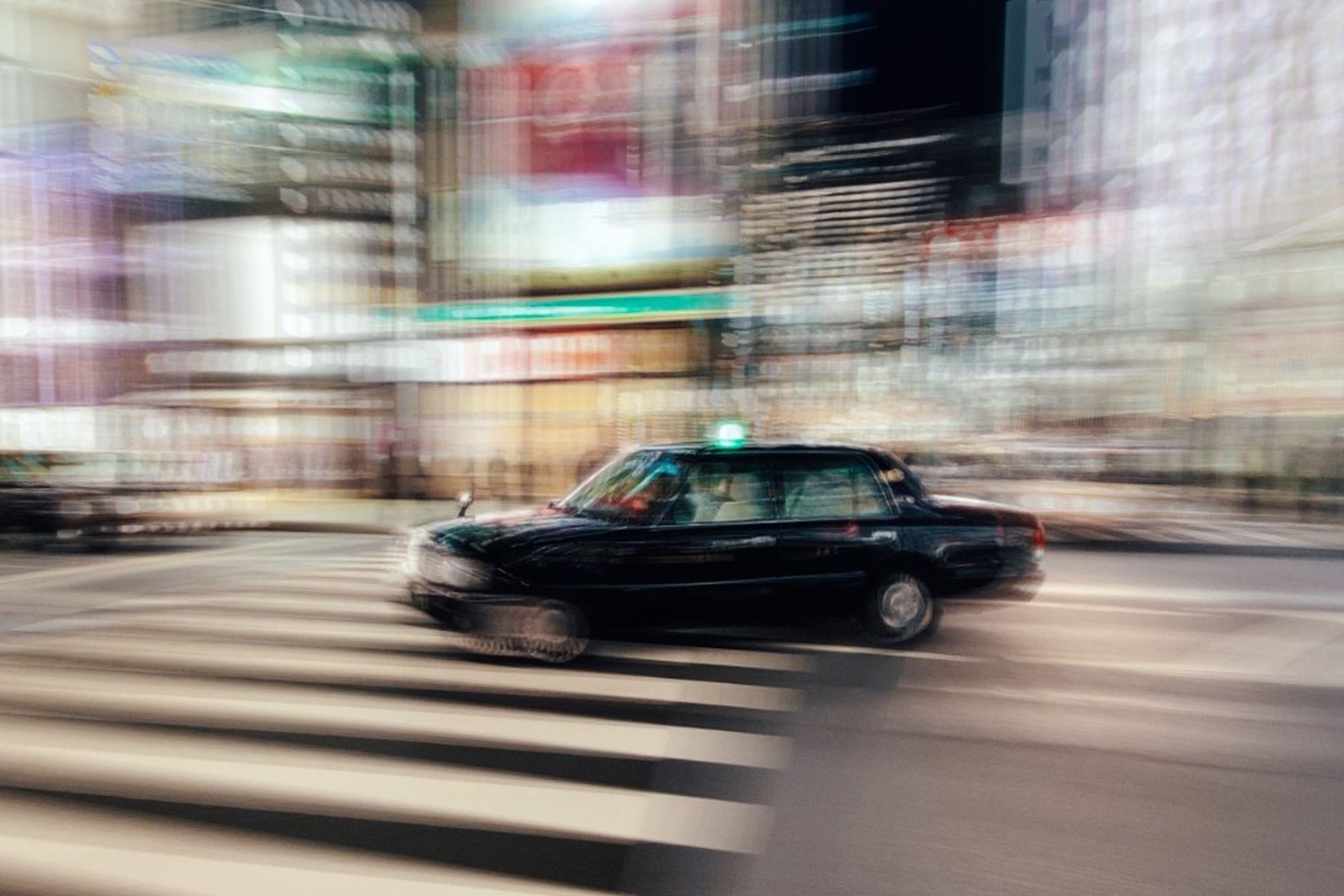 A black taxi panning through a night city, roof light a streak of green
